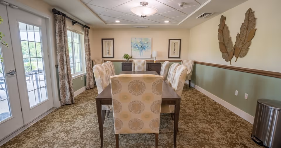 Dining room with a rectangular table surrounded by upholstered chairs, wall art, and glass doors leading to an outdoor area.