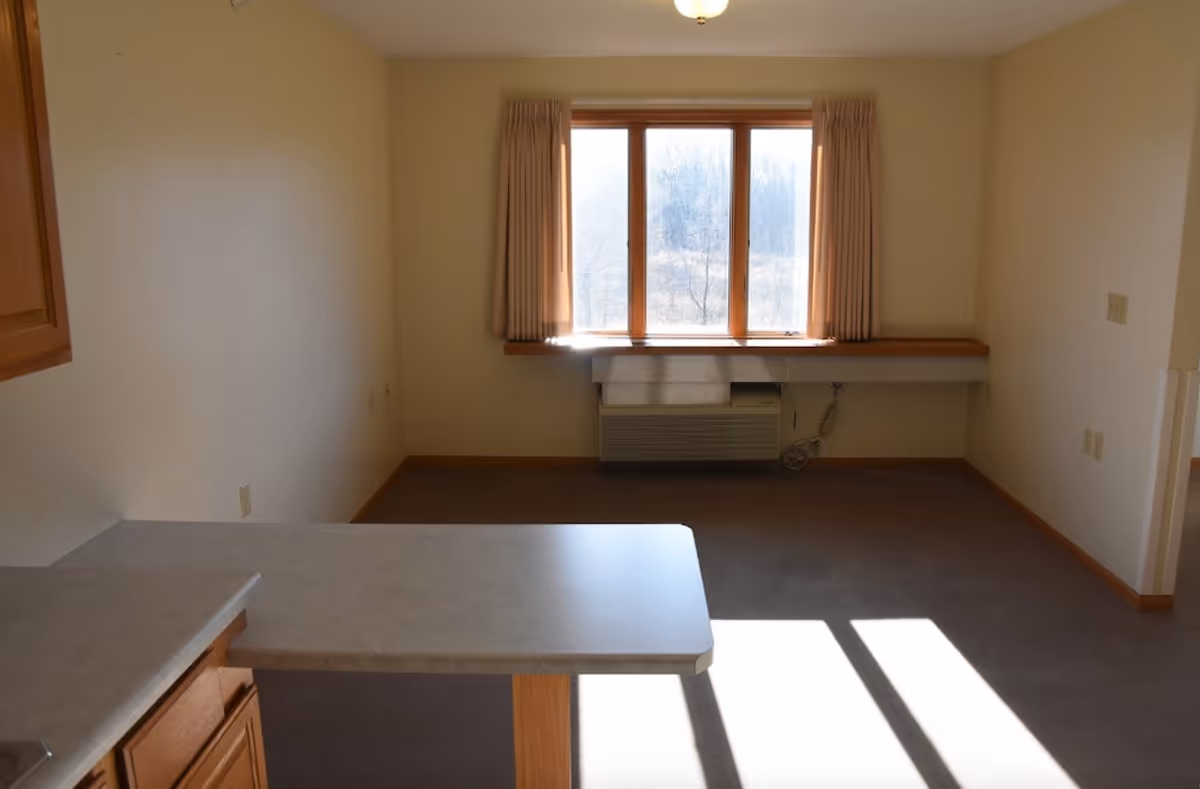 Empty living area with a countertop in the foreground, a window with curtains and an air-conditioner beneath it.