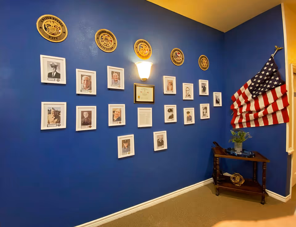 Blue interior wall displaying framed veteran photos and military emblems, an American flag, and a small wooden table.