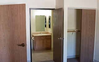View of a room with an open closet on the right and an open door leading to a bathroom with a sink, mirror, and wooden cabinet.