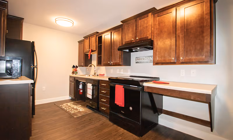 A modern kitchen with dark wood cabinets, black refrigerator and stove, a sink, and a fold-down countertop.