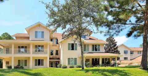 Two-story light-yellow senior living building with balconies on a sunny green lawn.