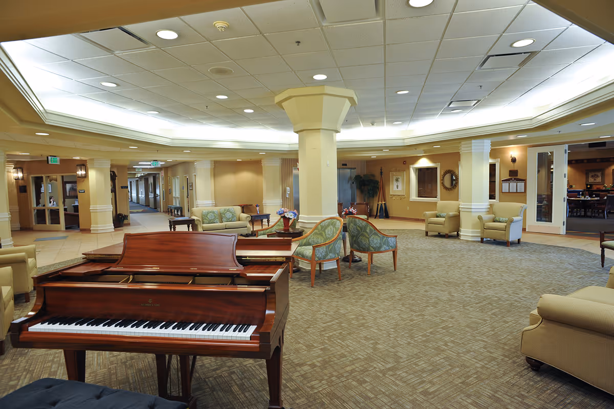 Spacious senior living community lounge with a grand piano, grouped seating, and soft overhead lighting.
