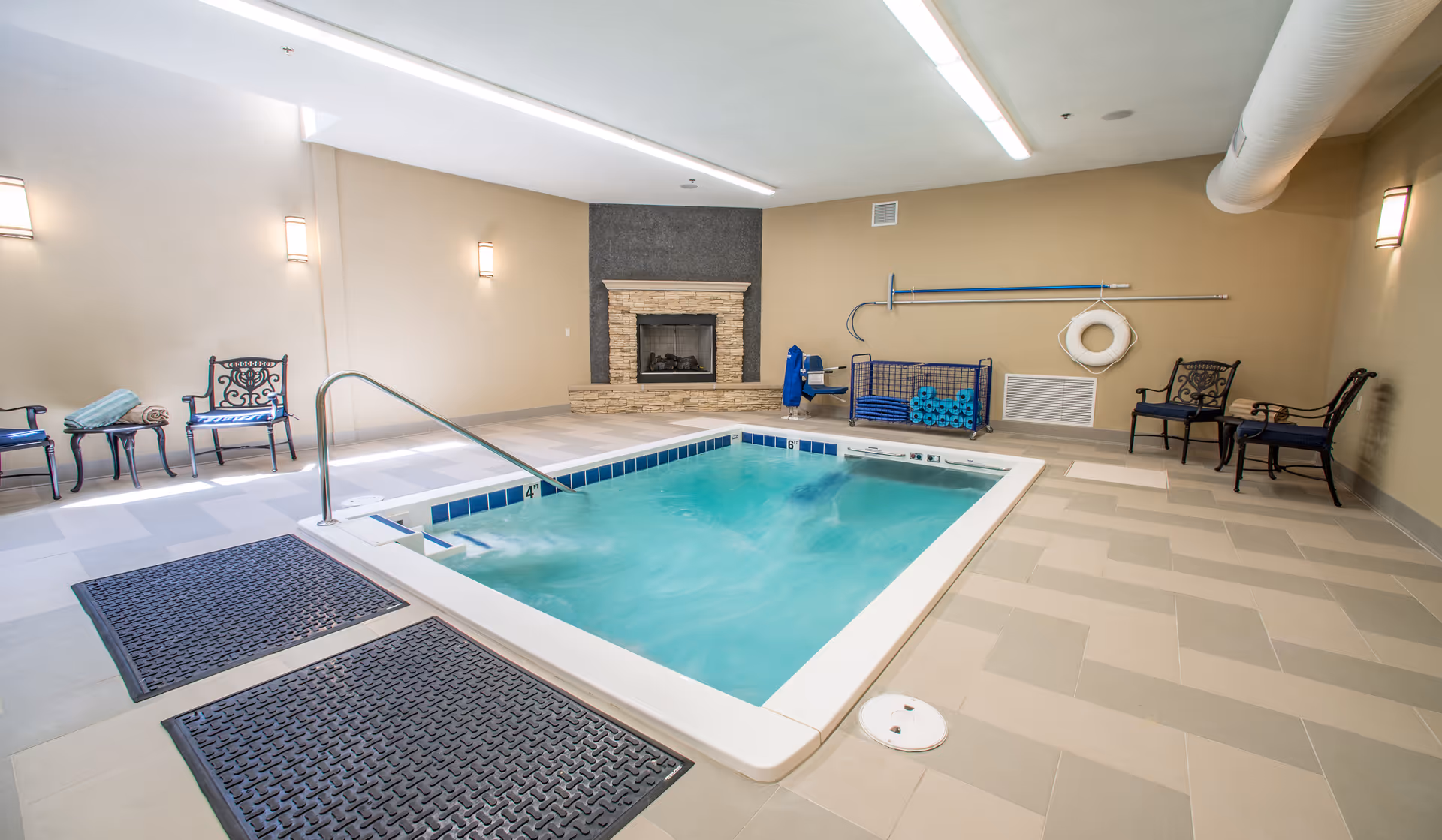 Indoor therapy pool area with bubbling spa, chairs, towels, a fireplace and a pool lift.