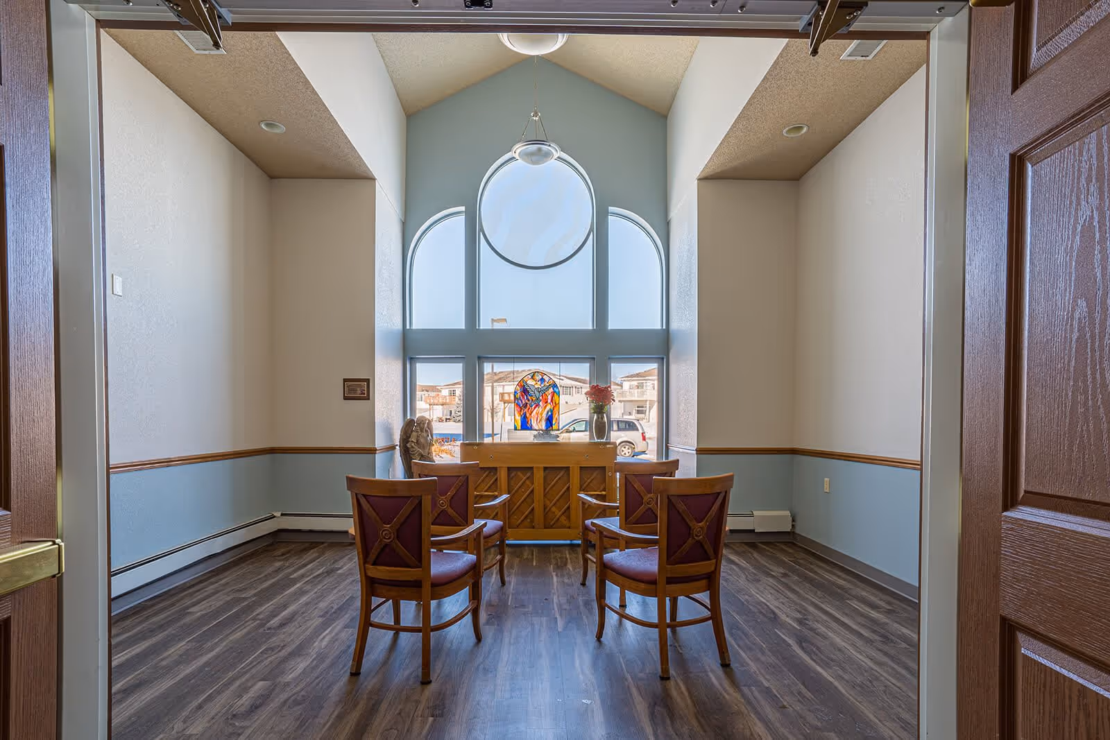 Small communal seating area with four chairs facing a piano beneath large arched windows and a hanging light.