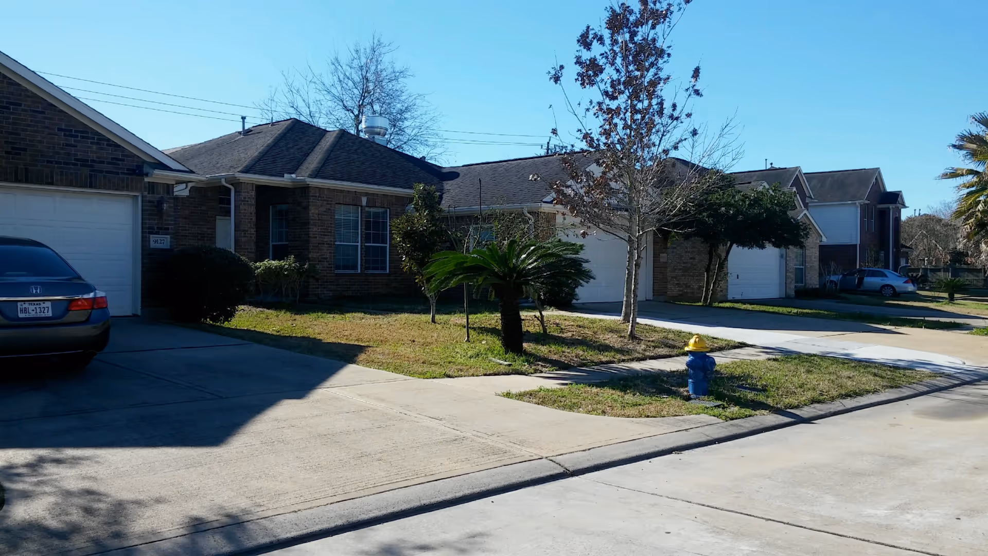Row of suburban brick houses with driveways, parked cars, small front lawns, and a blue fire hydrant.