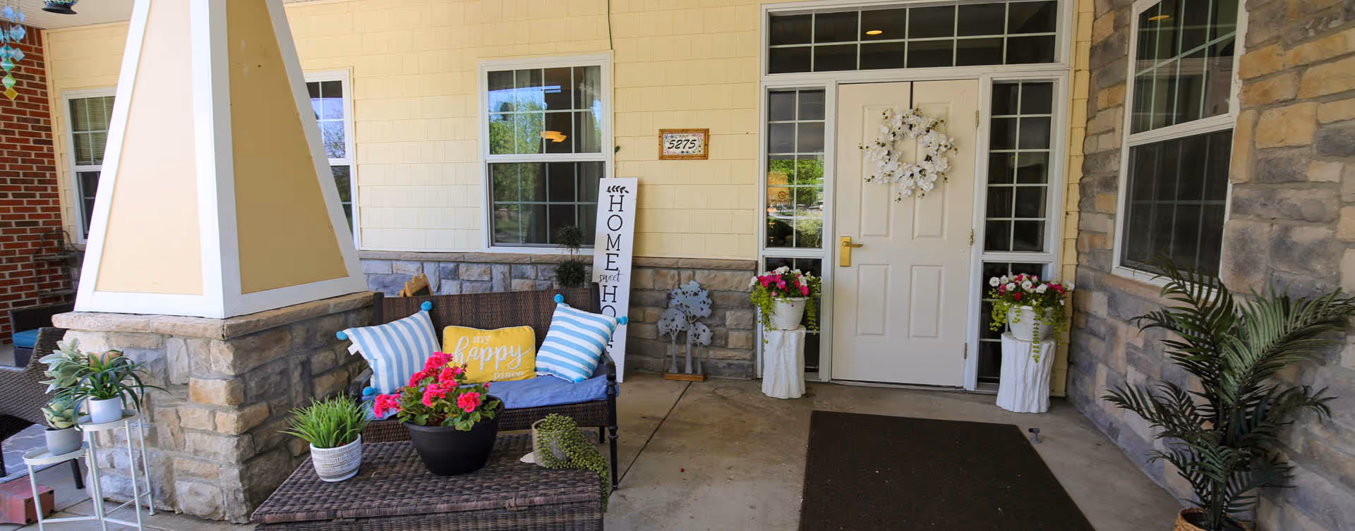 Covered front porch entrance with wicker seating, potted plants, and a white door decorated with a wreath.