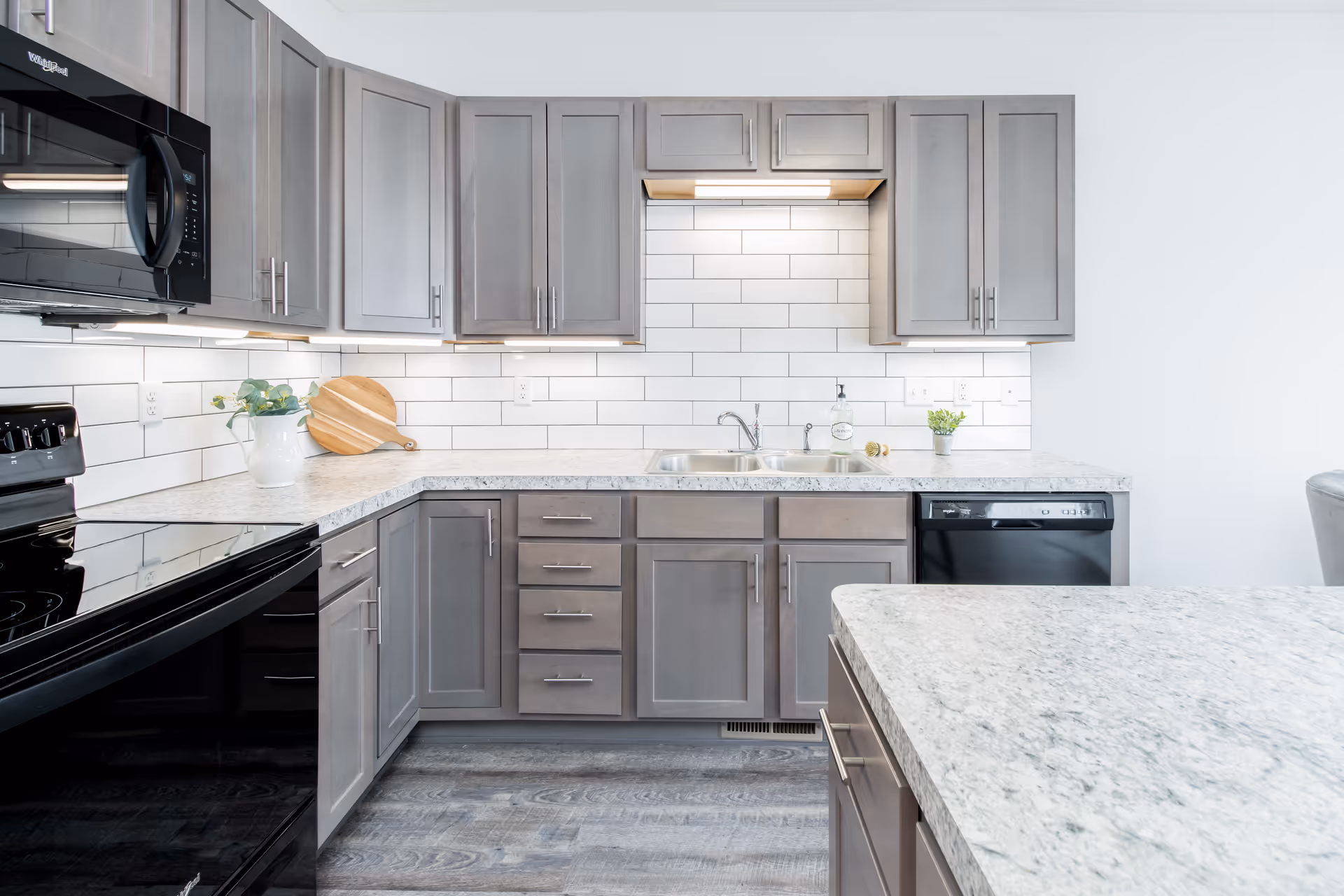 Modern kitchen featuring gray cabinets, white subway tile backsplash, marble countertops, a double sink and black appliances.