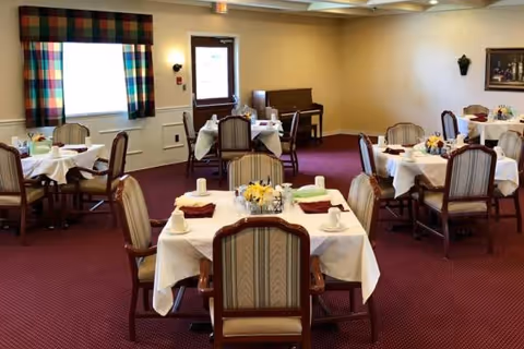 A senior living dining room with round tables, white tablecloths, and centerpieces.