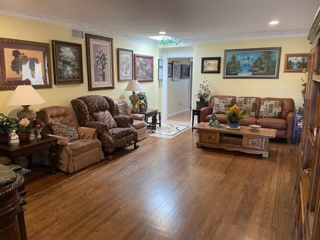 Spacious living room with sofas and armchairs arranged around a wooden coffee table, framed artwork on yellow walls, and hardwood floors.