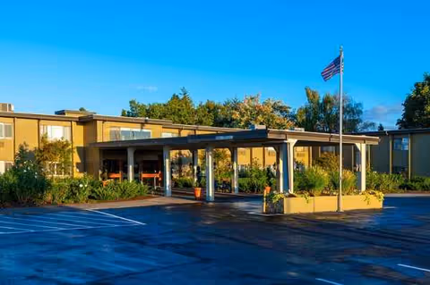 Senior living facility front entrance with a covered drive-up, parking lot, and American flag.