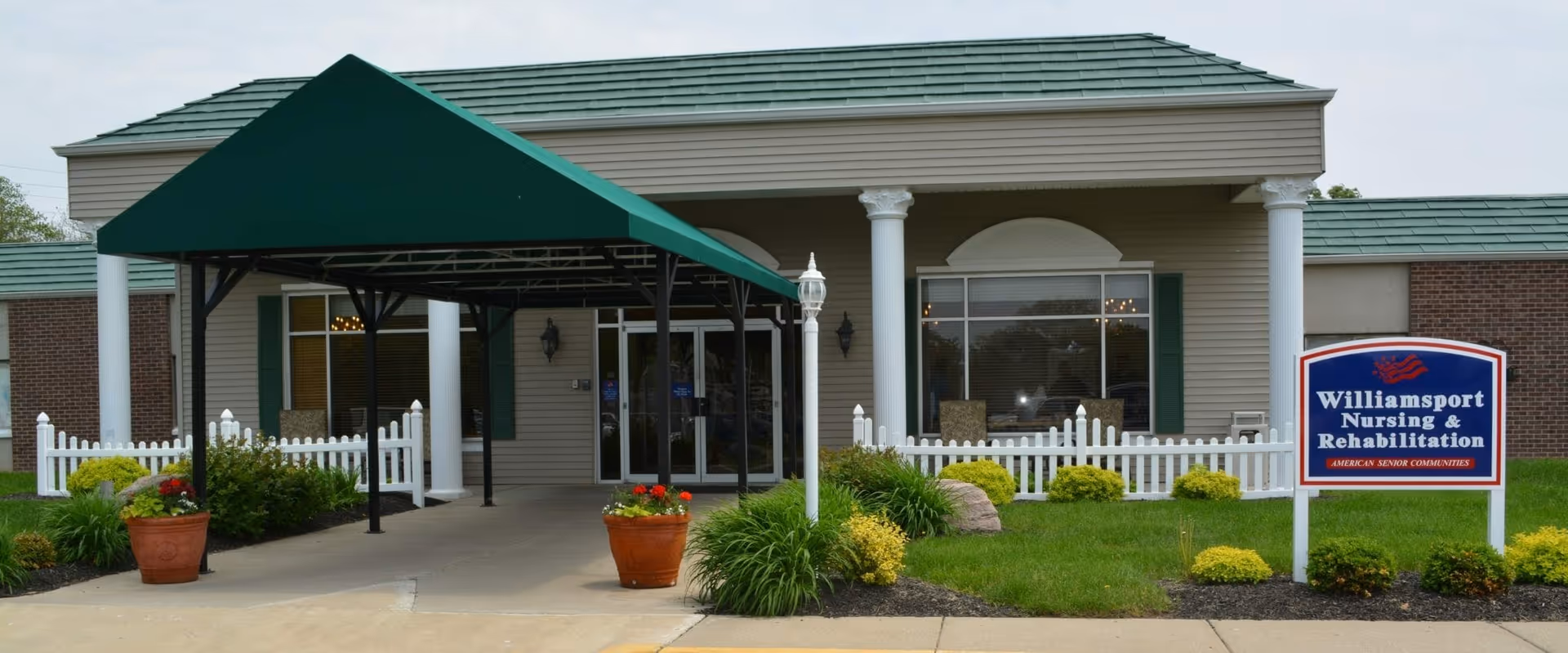 Front entrance of Williamsport Nursing & Rehabilitation featuring a covered drop-off, white columns, landscaping, and a sign.