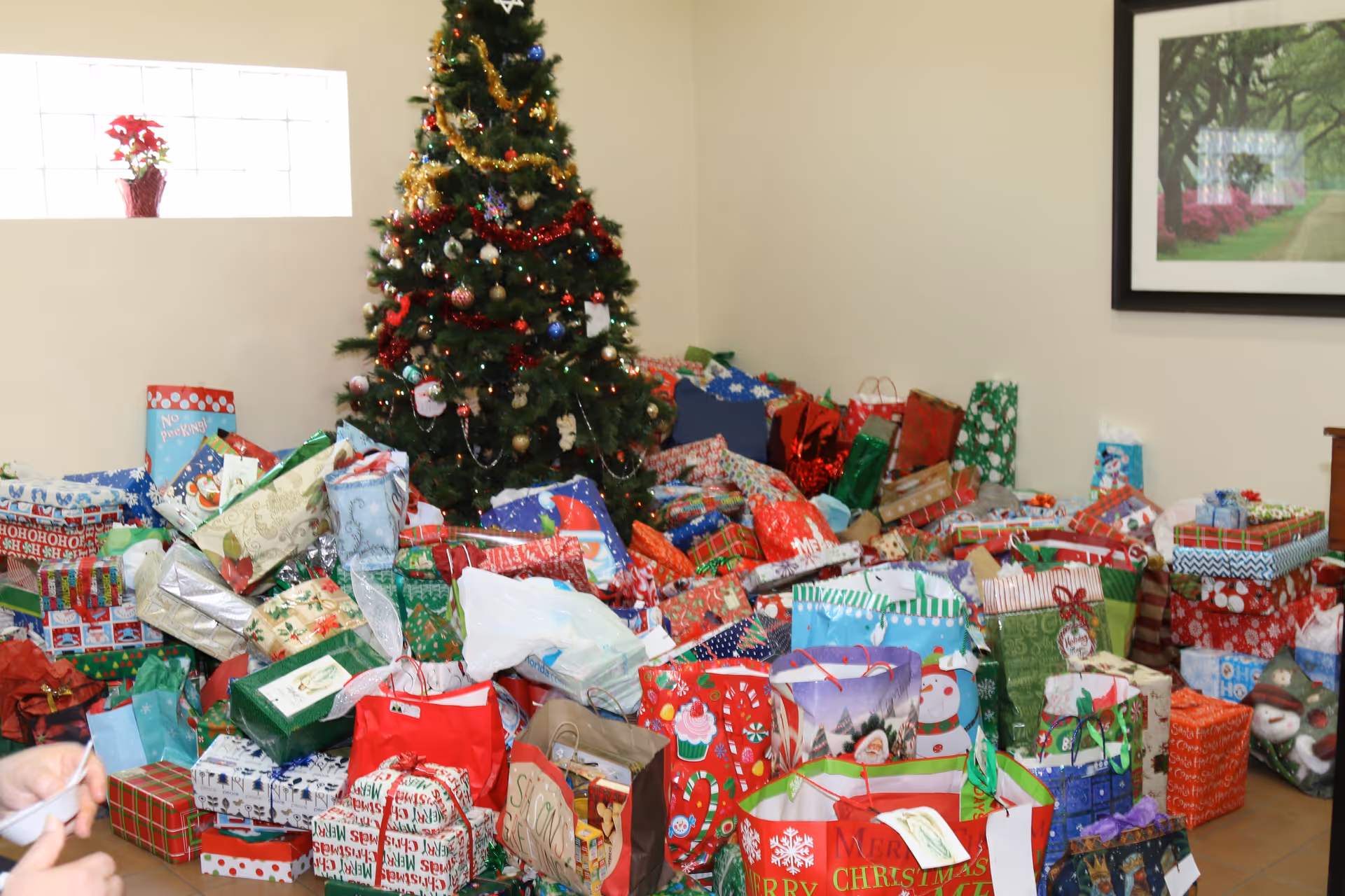 A decorated Christmas tree surrounded by a large pile of wrapped holiday presents in a room.