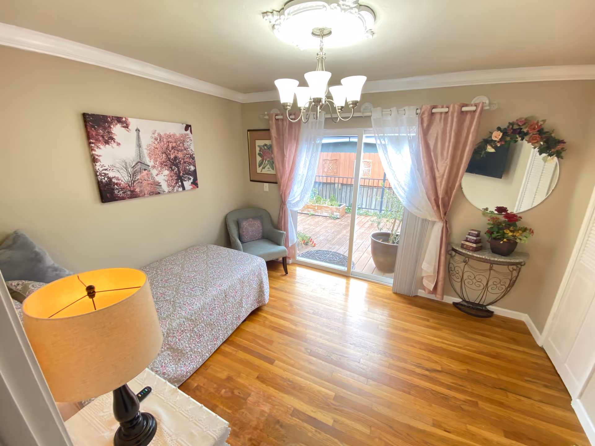 Bright single bedroom with a twin bed, armchair, lamp, hardwood floors and sliding glass doors leading to a small patio.
