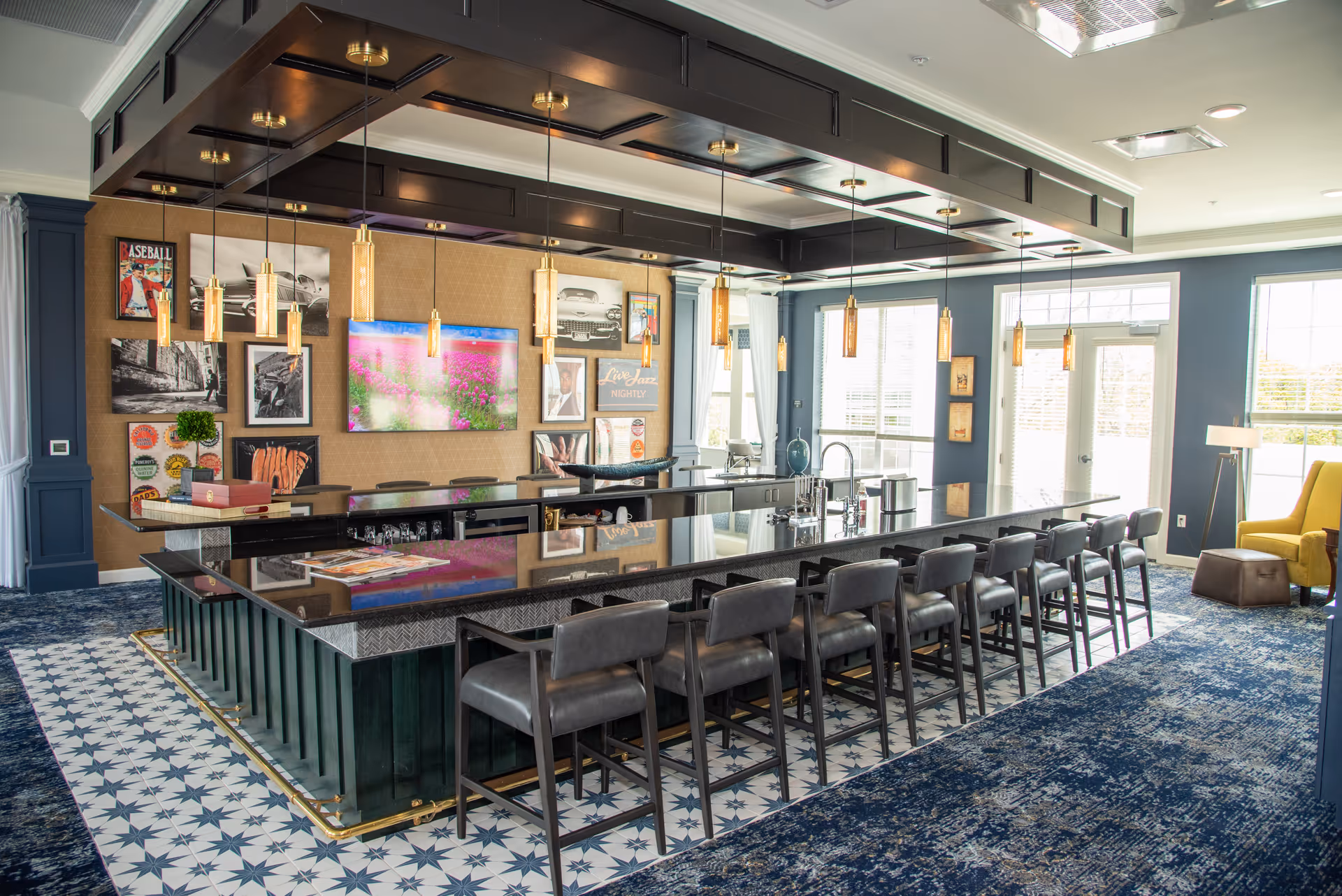 Bright common area with a long central black countertop island, pendant lights, and a row of barstools.