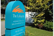 Outdoor view of a teal sign for The Lafayette, a rehabilitation and skilled nursing facility, situated on a grassy area with trees and a white fence in the background.