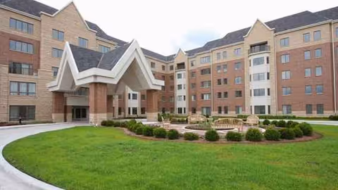 Front exterior view of Park Place of Elmhurst with brick buildings, entry canopy, and manicured lawn.