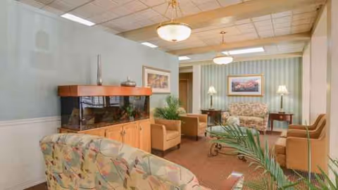 Senior living lounge with sofas, coffee tables, lamps, and framed art in pastel decor.