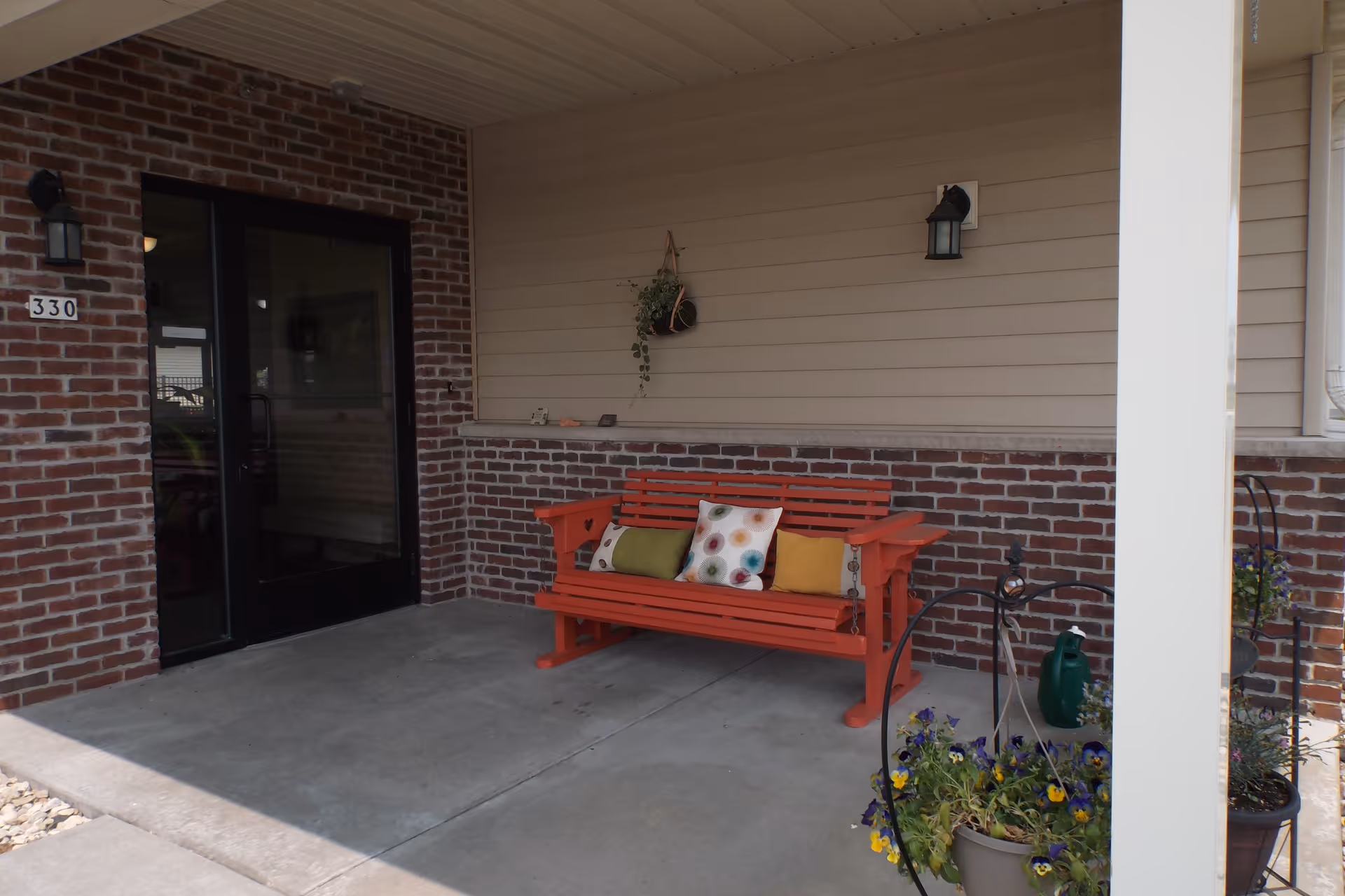 Covered front porch with a red bench with colorful pillows, potted flowers, and a glass entrance door marked 330.