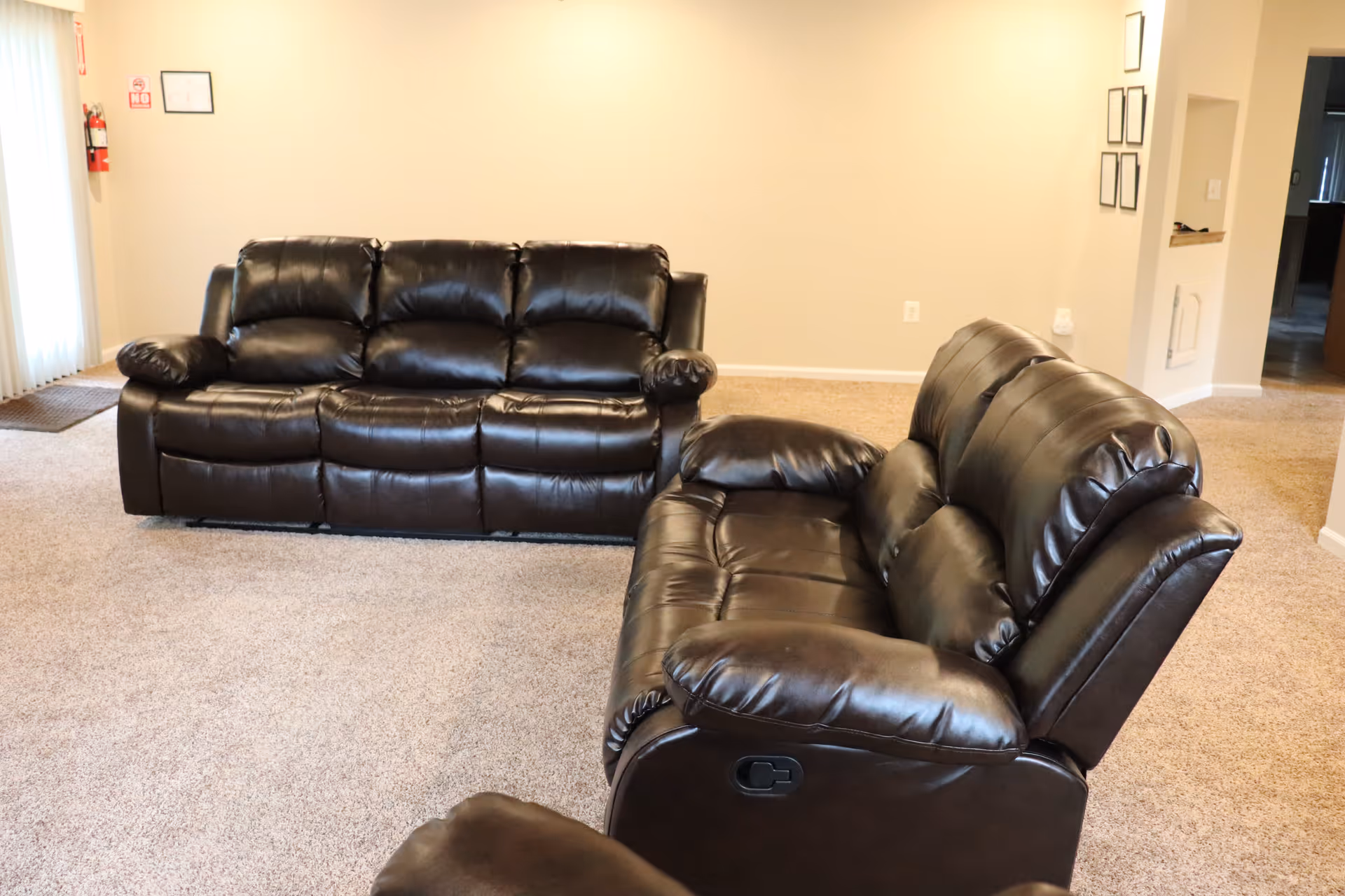 Two dark brown leather reclining sofas arranged in a carpeted living room with beige walls.