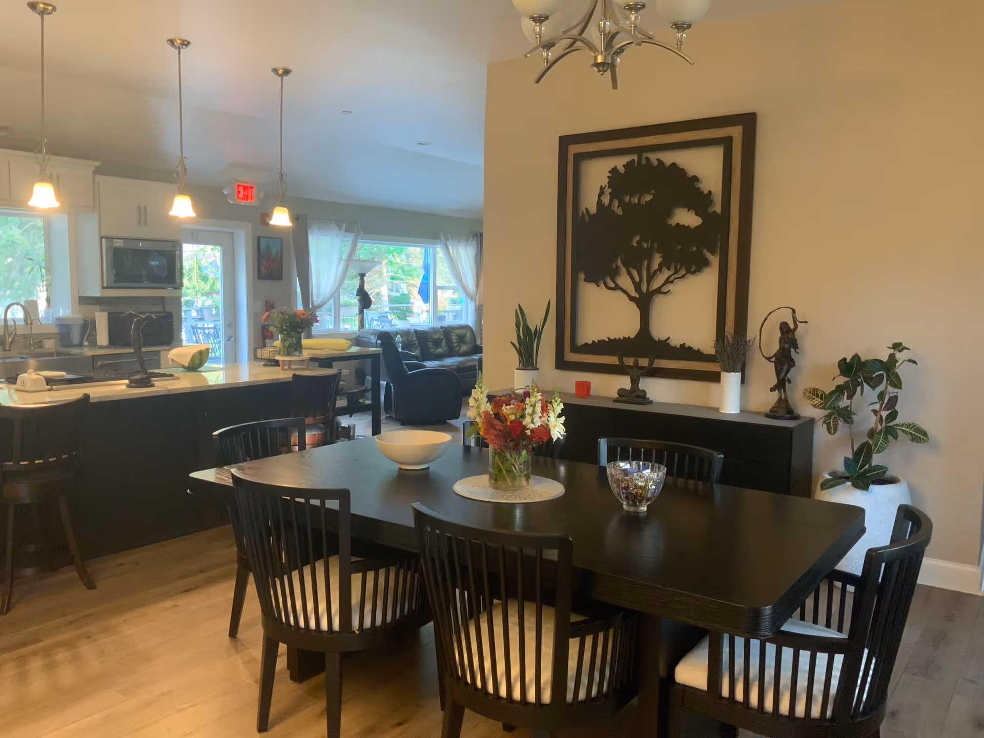 Dark dining table and chairs in a bright senior living dining area with a kitchen behind.