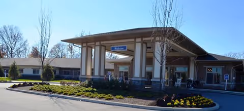 Exterior view of Countryside Meadows facility entrance with a covered drop-off area, landscaped flower beds, and leafless trees under a clear blue sky.