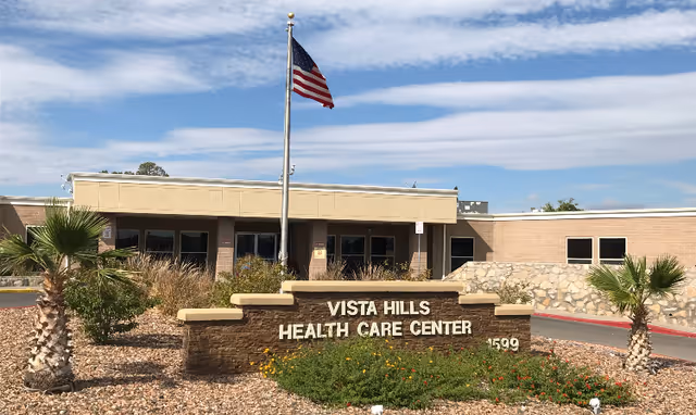 Front entrance of Vista Hills Health Care Center with a stone sign, American flag, and landscaped driveway.