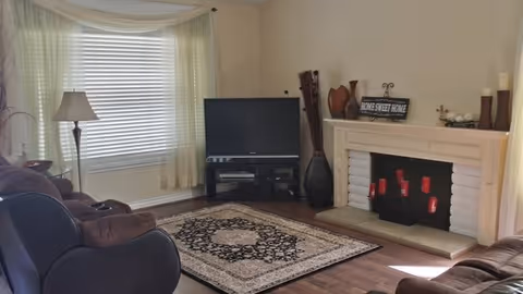 Cozy living room in South Home Care with sofa, rug, TV, and fireplace.