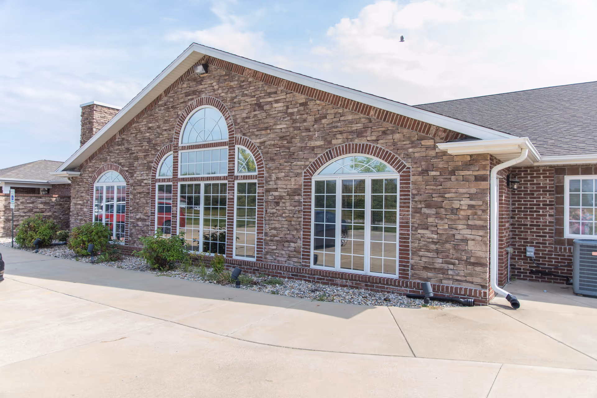 Exterior view of a brick senior living facility with large windows and landscaping.