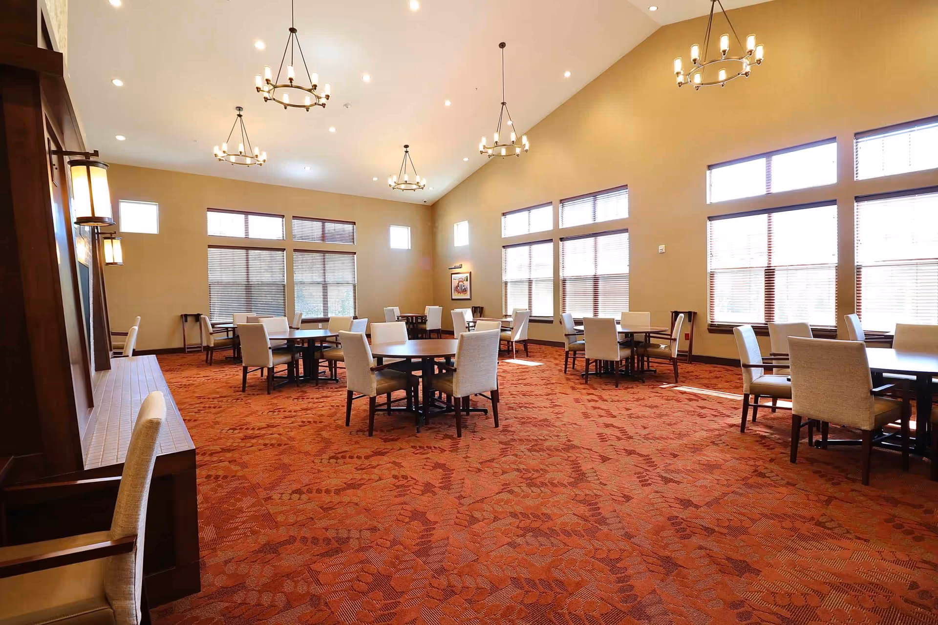 Spacious dining room with round tables, upholstered chairs, large windows and chandeliers.