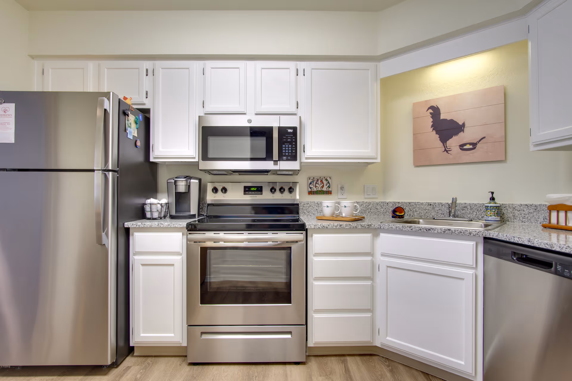 Bright modern kitchen with stainless steel refrigerator, stove and microwave, white cabinets and granite countertops.