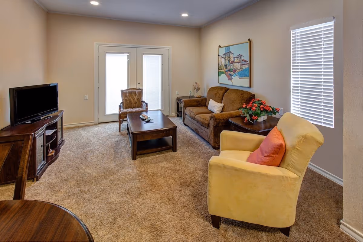 Carpeted living room with a sofa, armchairs, coffee table, TV stand, and French doors.