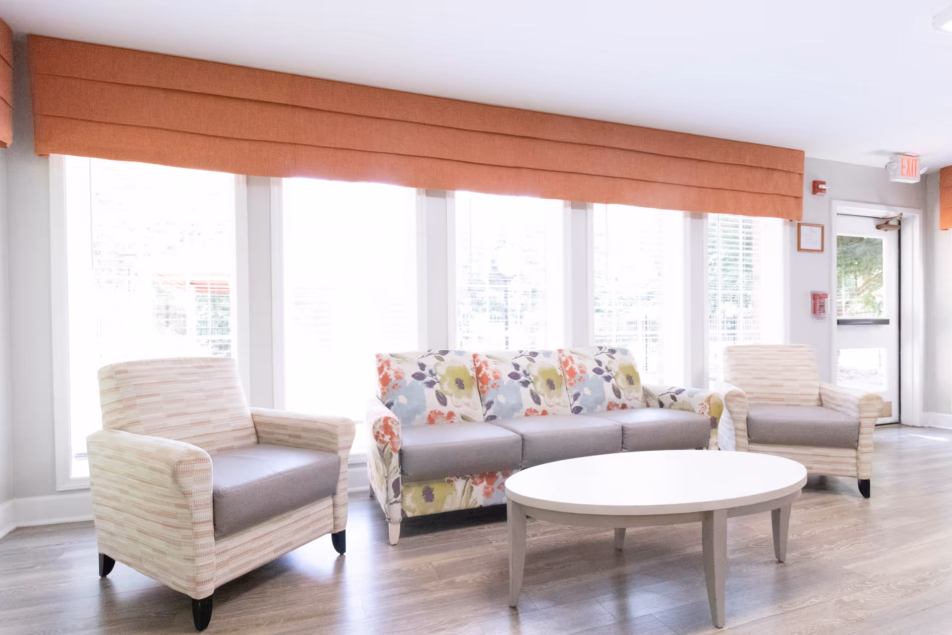 Bright seating area with a floral sofa, two armchairs and a round coffee table in front of large windows.