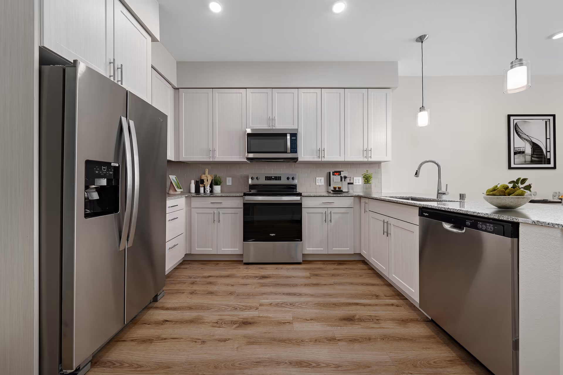 Modern open kitchen with stainless steel appliances, white cabinets, a granite countertop island, and wood-look flooring.