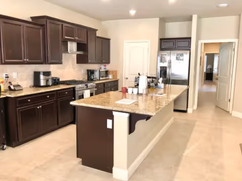Spacious kitchen with granite island, dark wood cabinets, and stainless steel appliances.