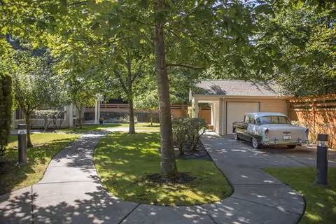 Tree-lined walkway curves past lawn to a garage with a vintage car.