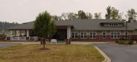 Single-story brick senior living facility with a driveway, entrance, and front lawn.