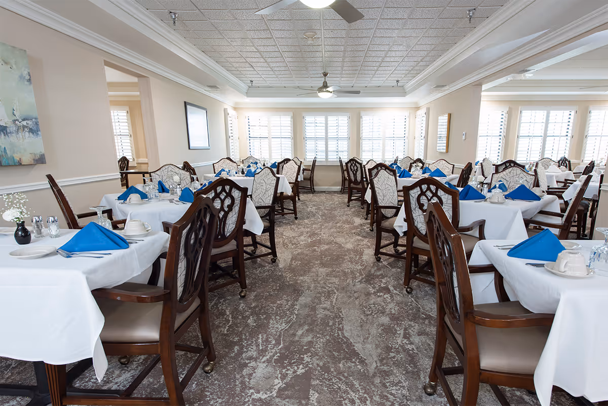 Bright dining room with rows of tables set with white linens and blue napkins.