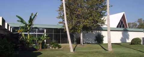 Exterior view of Carlton Shores Health and Rehab Center with lawn, trees, and large windows.