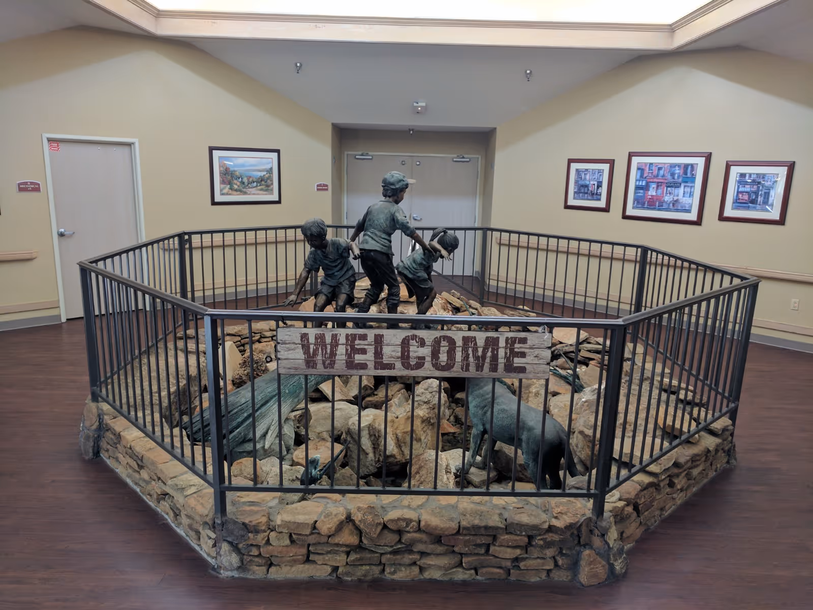 Indoor lobby area featuring a fenced stone sculpture of children and animals with a 'WELCOME' sign.