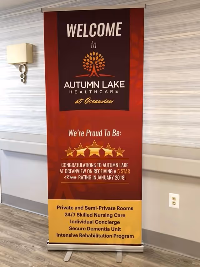 A freestanding red and yellow welcome banner for Autumn Lake Healthcare at Oceanview displayed against a hallway wall.