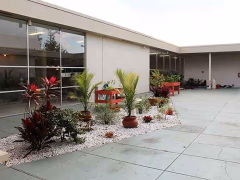 Outdoor courtyard of a senior living center with potted plants, white rocks, and red seating.