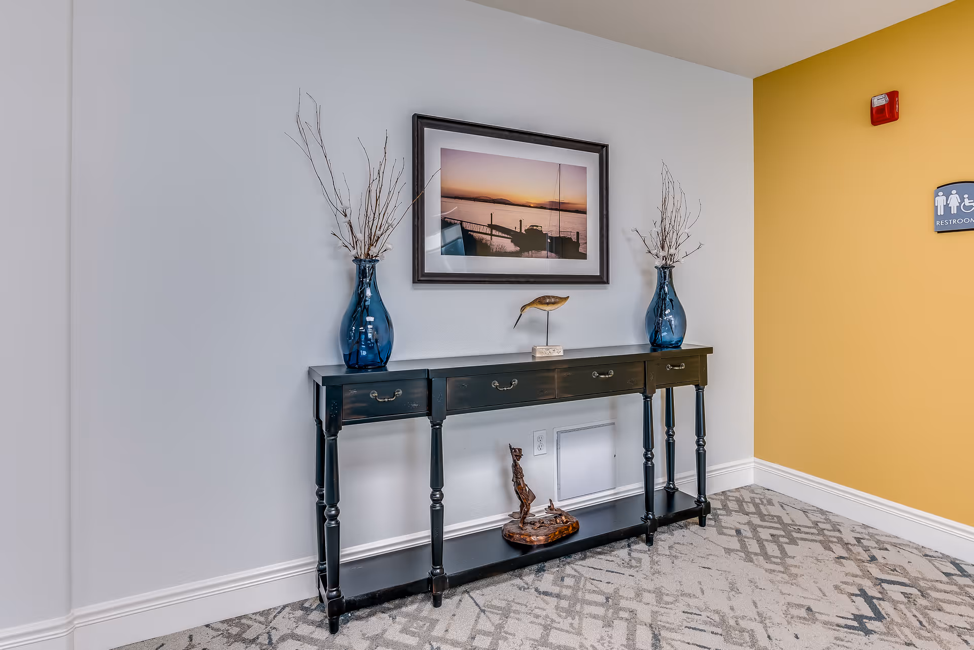 Console table topped with blue vases and a framed sunset photo against a hallway wall.