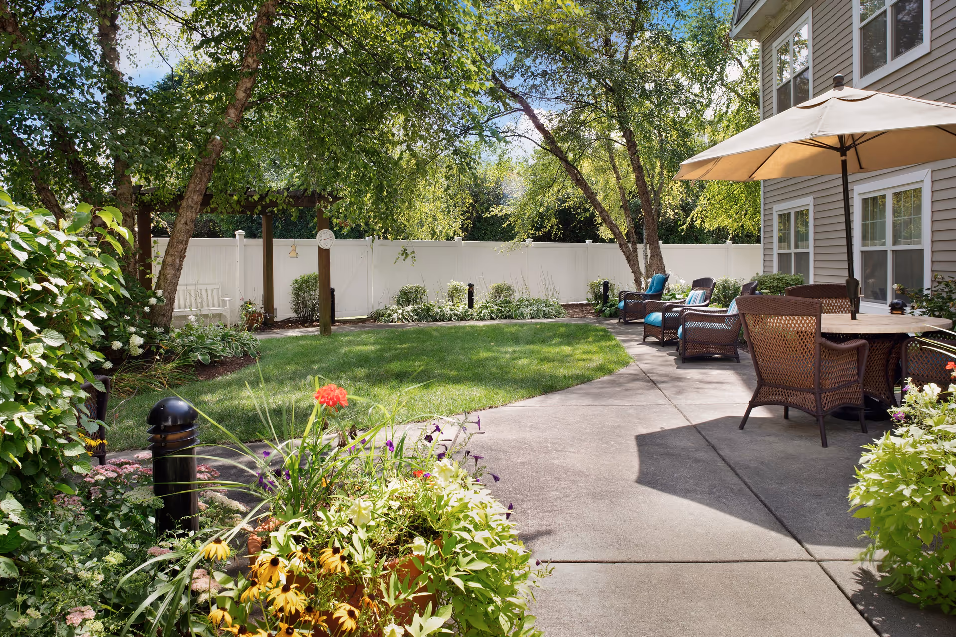 Sunny outdoor patio and grassy yard with wicker seating, a dining table and umbrella next to a residential building.