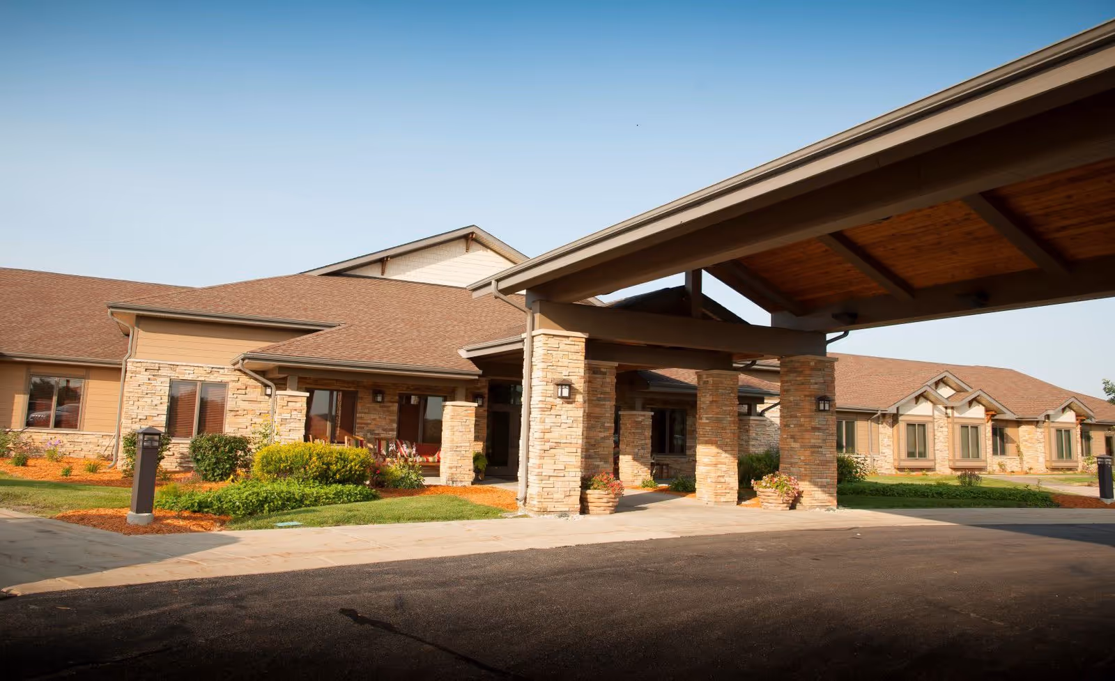 Exterior view of a senior living facility named NorthPointe Terrace, showing a covered entrance supported by stone pillars, landscaped greenery, and a clear sky.