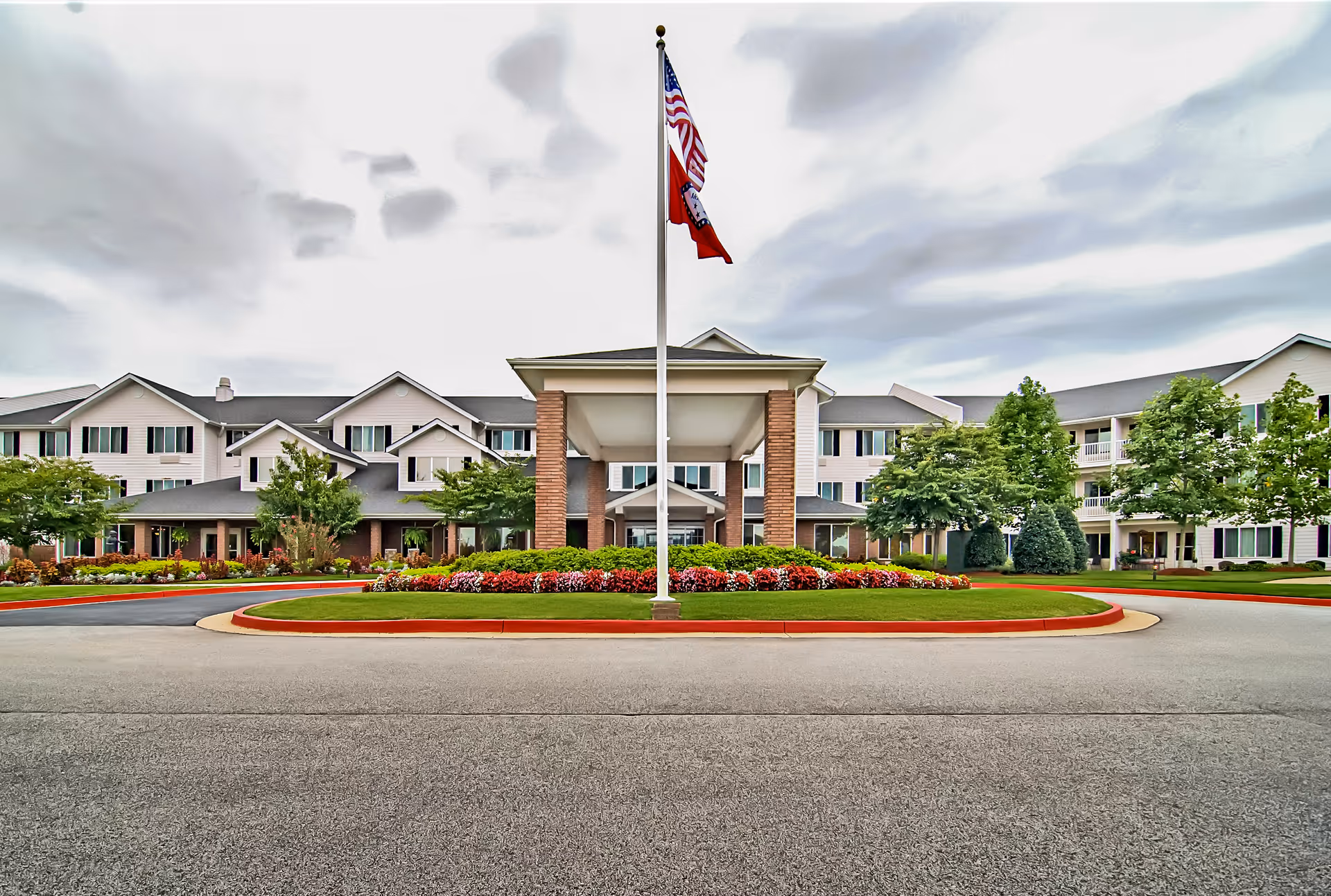 Front exterior view of Morada Fort Smith facility with a circular driveway, landscaped flower beds, and two flags on a flagpole in the center.