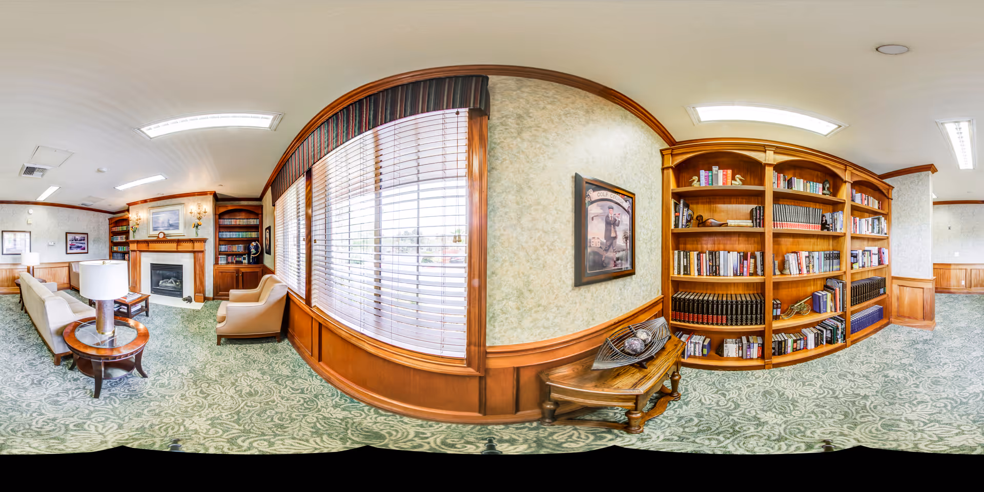 Bright senior living lounge with sofas, a fireplace, large window blinds and built-in wooden bookshelves.