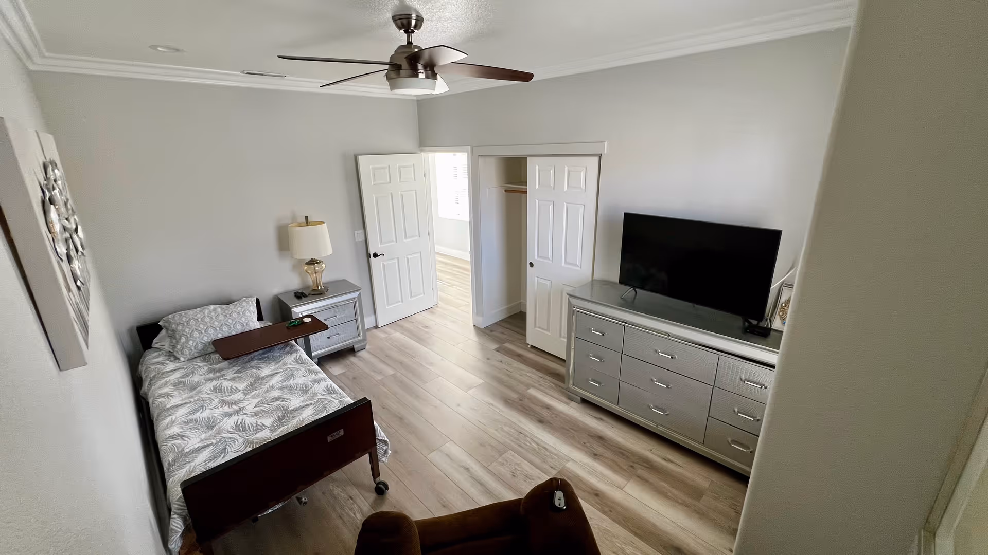 Bright bedroom with a single bed, nightstand and lamp, dresser with a TV, and a ceiling fan.