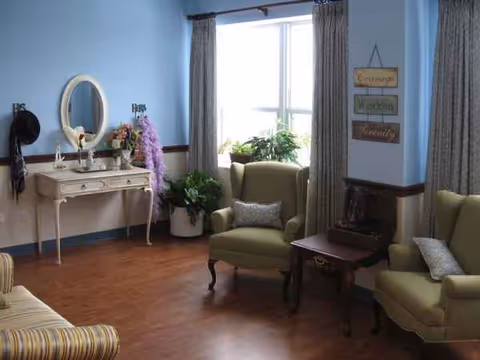 Cozy senior living lounge with green chairs, plants, and a vanity.
