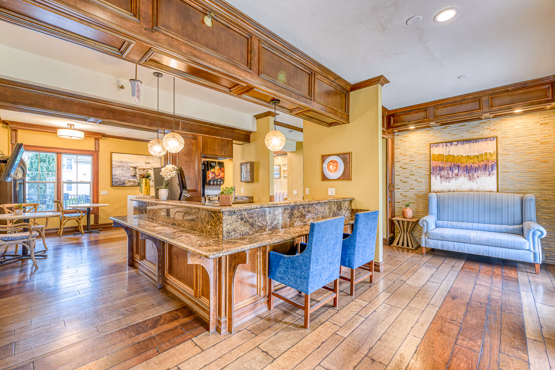 Bright common-area interior with a marble-topped reception counter, blue chairs, pendant lights and a seating area with a blue sofa.